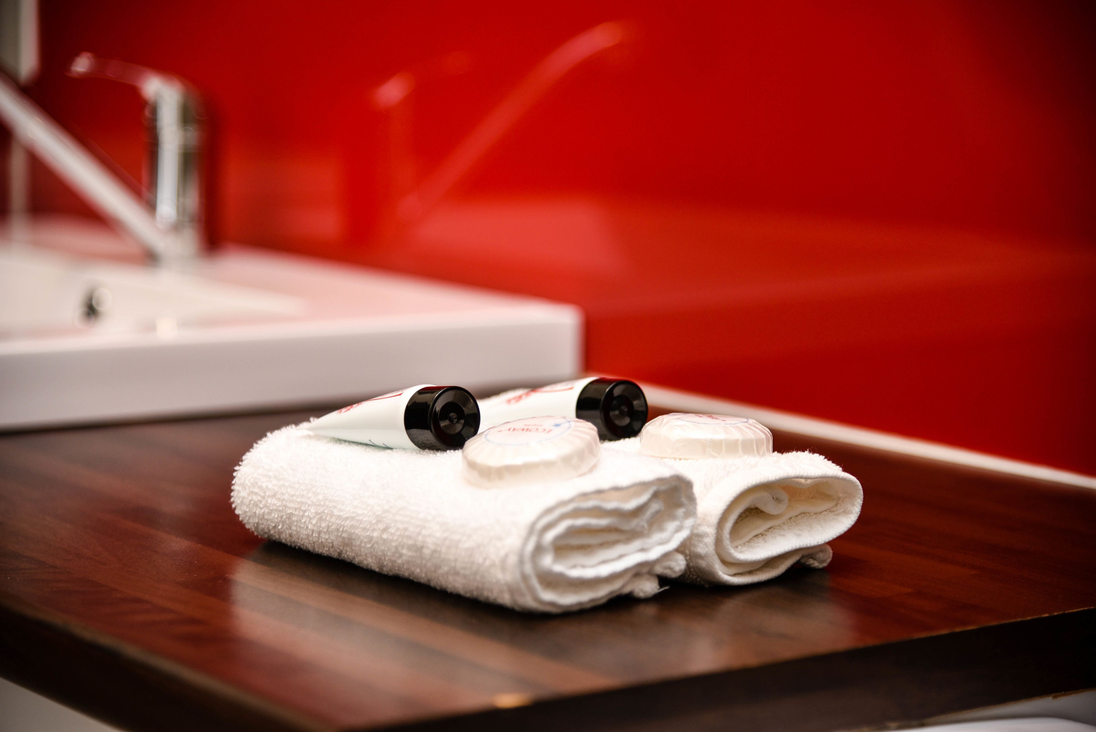 A neatly folded white towel with two black caps on a wooden surface in a bathroom with a red wall.