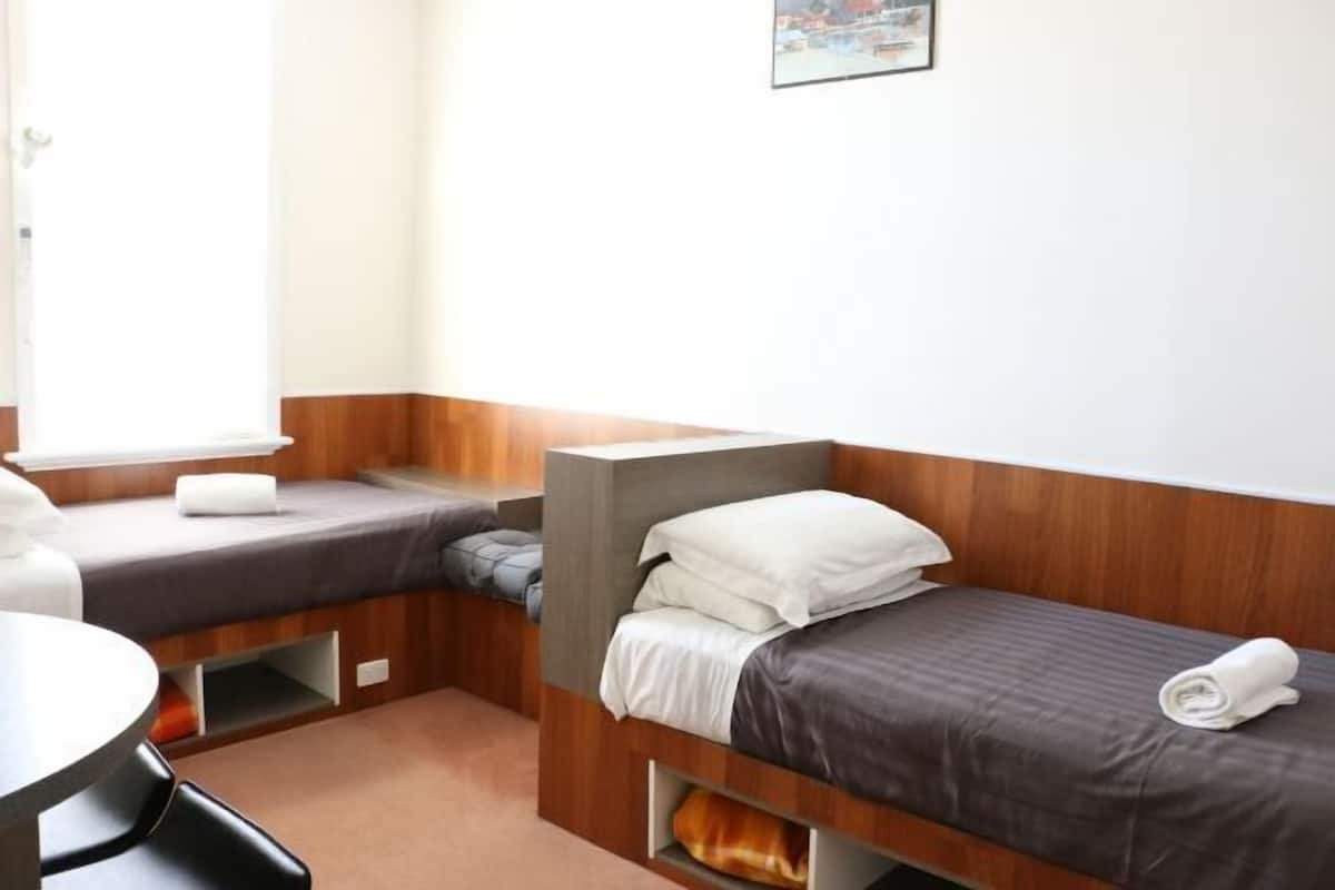 Two single beds with wooden headboards and grey bedding, a small table and chair for dining or working.