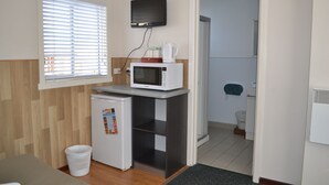 A compact kitchenette with a microwave, a small refrigerator, and a television mounted above the counter. - Hobart Tower Motel (New Town)