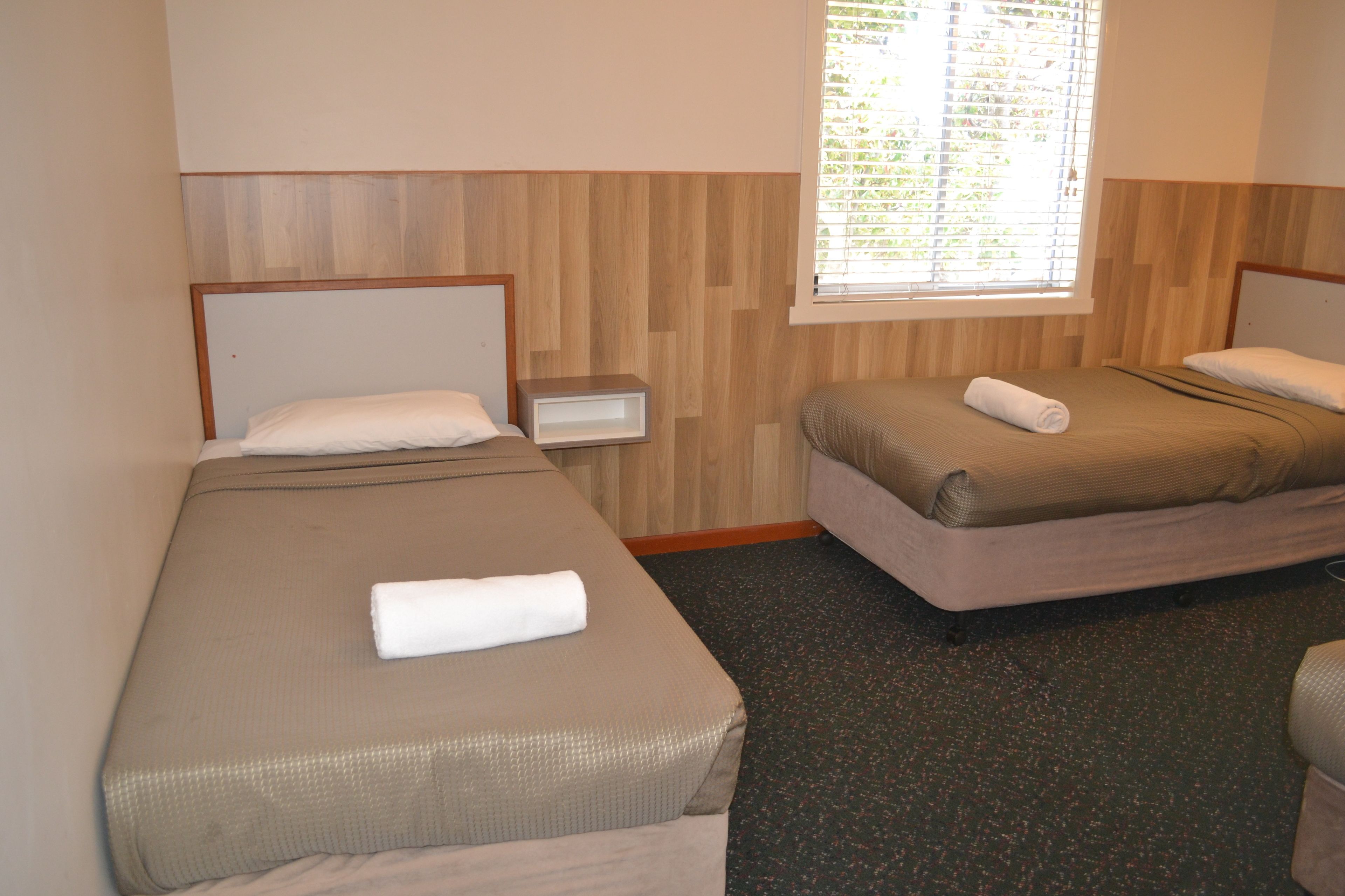 A hotel room with two beds, a nightstand, and a window with blinds.
