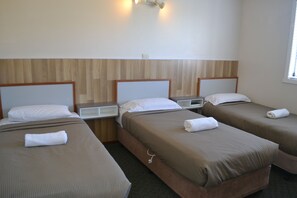 Habitación de hotel con tres camas individuales, cada una con cabecera de madera y una mesita de noche pequeña.