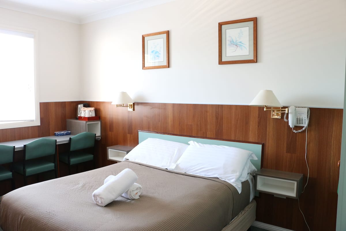 Ein Hotelzimmer mit Bett, zwei Stühlen, einem Schreibtisch, einem Nachttisch und einem Telefon.