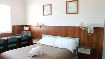 A hotel room with a bed, two chairs, a desk, a nightstand, and a telephone.