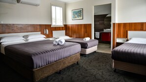 A hotel room with two beds, a wooden headboard, a painting on the wall, and a bathroom visible through an open door. - Hobart Tower Motel (New Town)