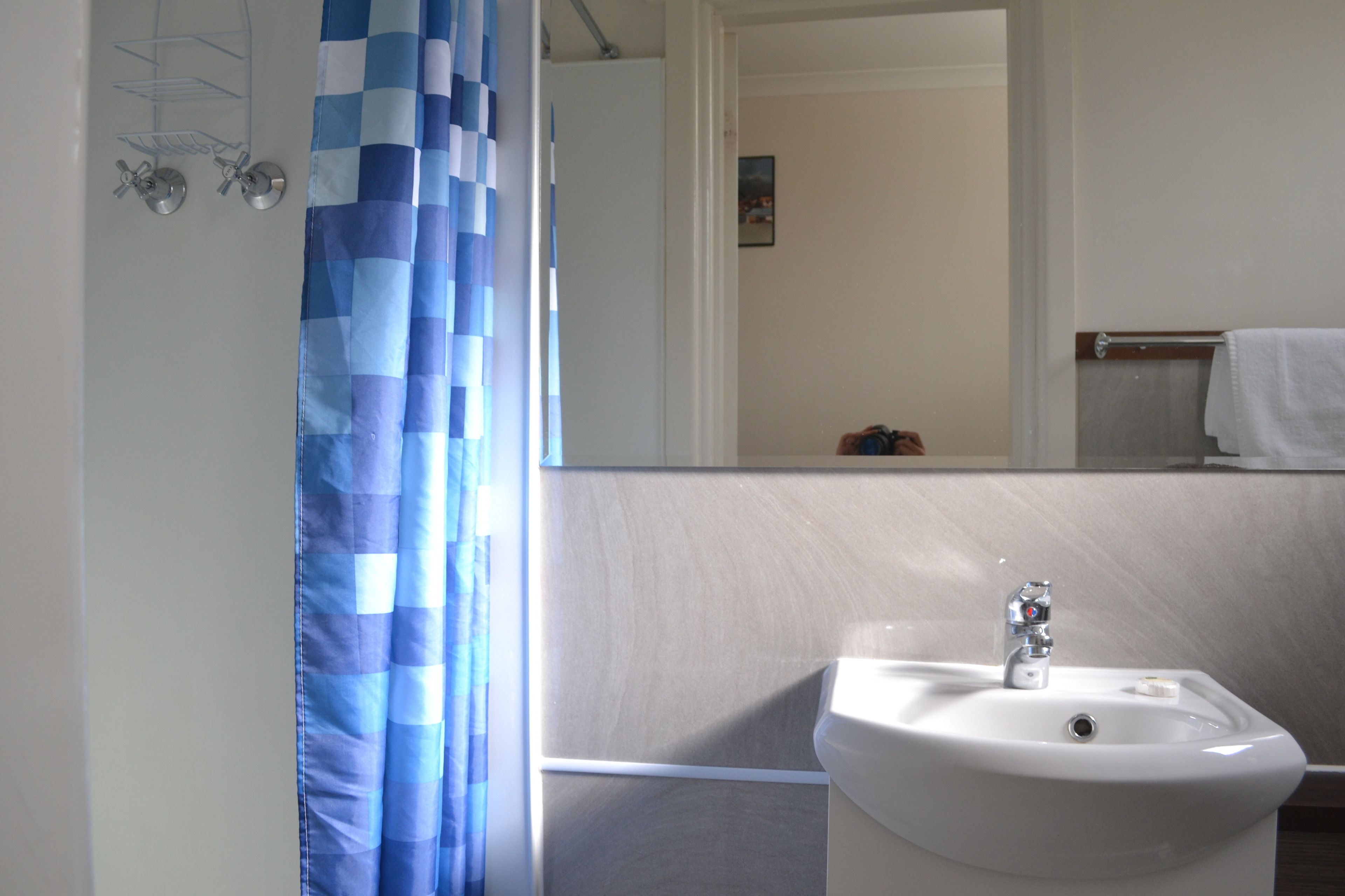 Un baño con lavabo blanco, un espejo y una cortina de ducha azul a cuadros.