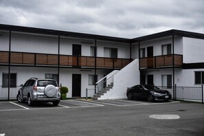 Un edificio moderno con dos espacios para estacionamiento, una escalera y un coche negro estacionado a la derecha.