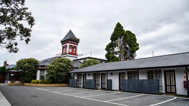 A motel with a prominent tower, a parking lot, and a building with a dark roof. - Hobart Tower Motel (New Town)