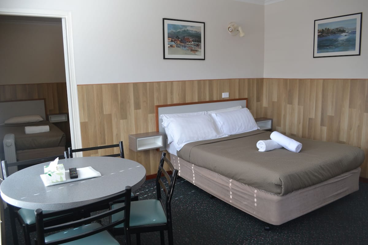 Ein Hotelzimmer mit einem Bett, einem runden Tisch mit Stühlen, einem Nachttisch und zwei gerahmten Bildern an der Wand.