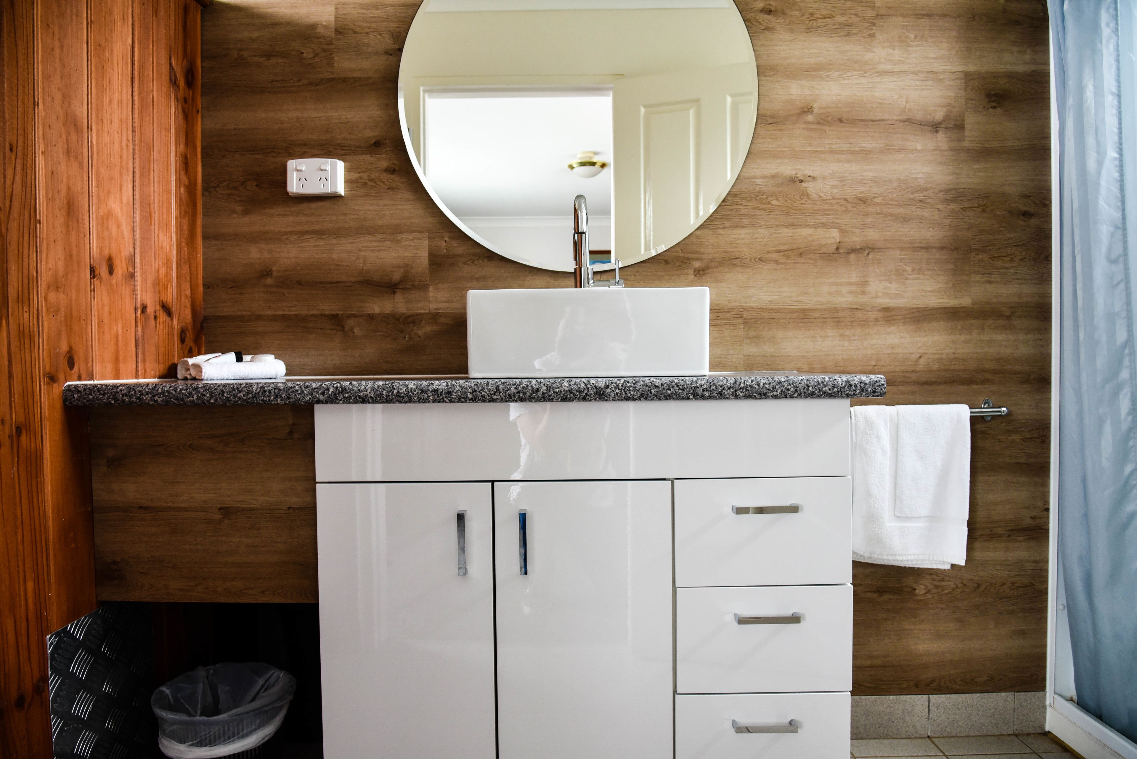 Un baño con pared de madera, lavamanos blanco, espejo y barra para toallas.