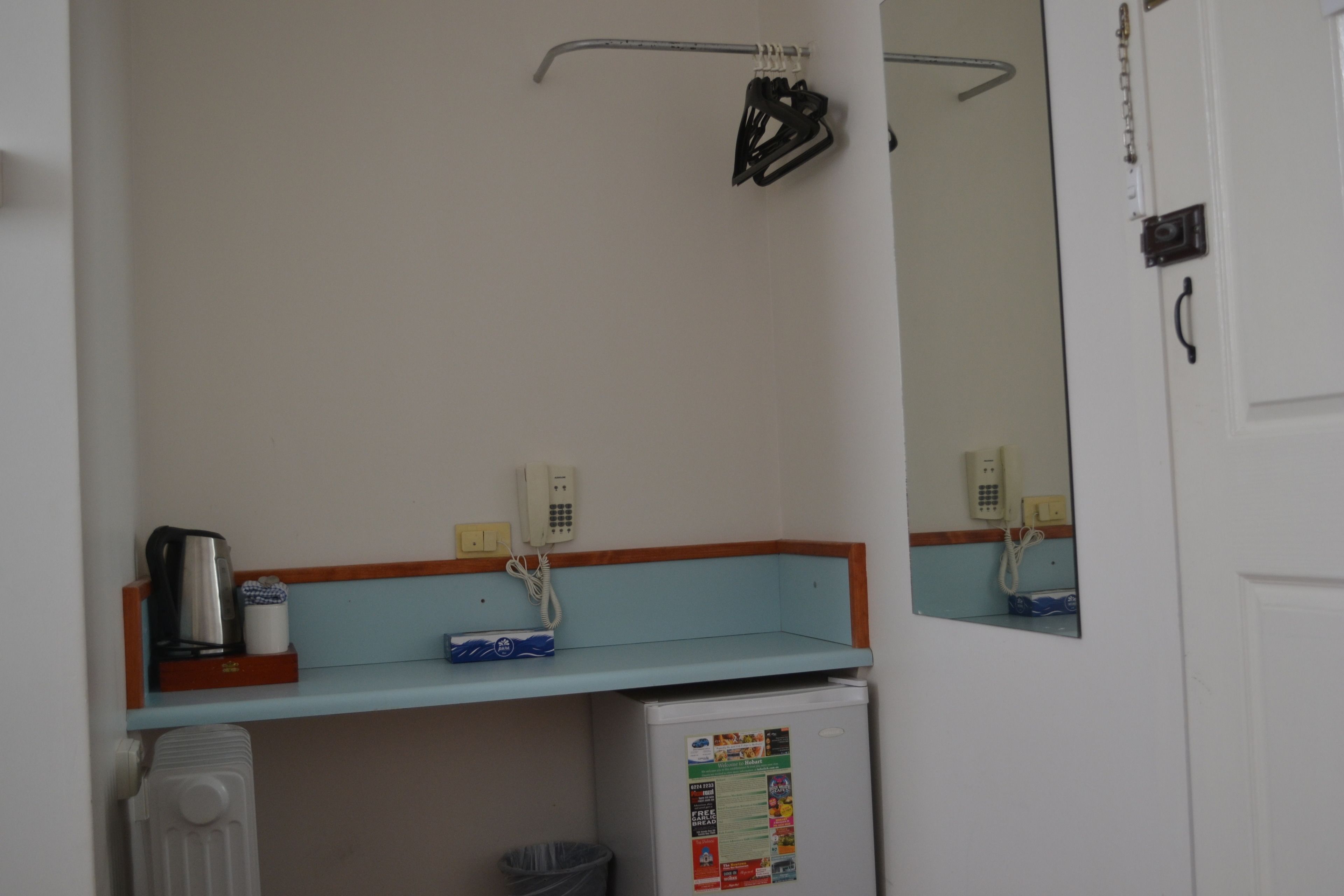 A bathroom with a white sink, a mirror, a small shelf with a coffee maker, and a refrigerator.
