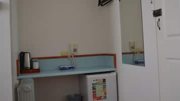 A bathroom with a white sink, a mirror, a small shelf with a coffee maker, and a refrigerator.