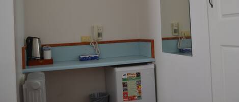 A bathroom with a white sink, a mirror, a small shelf with a coffee maker, and a refrigerator.