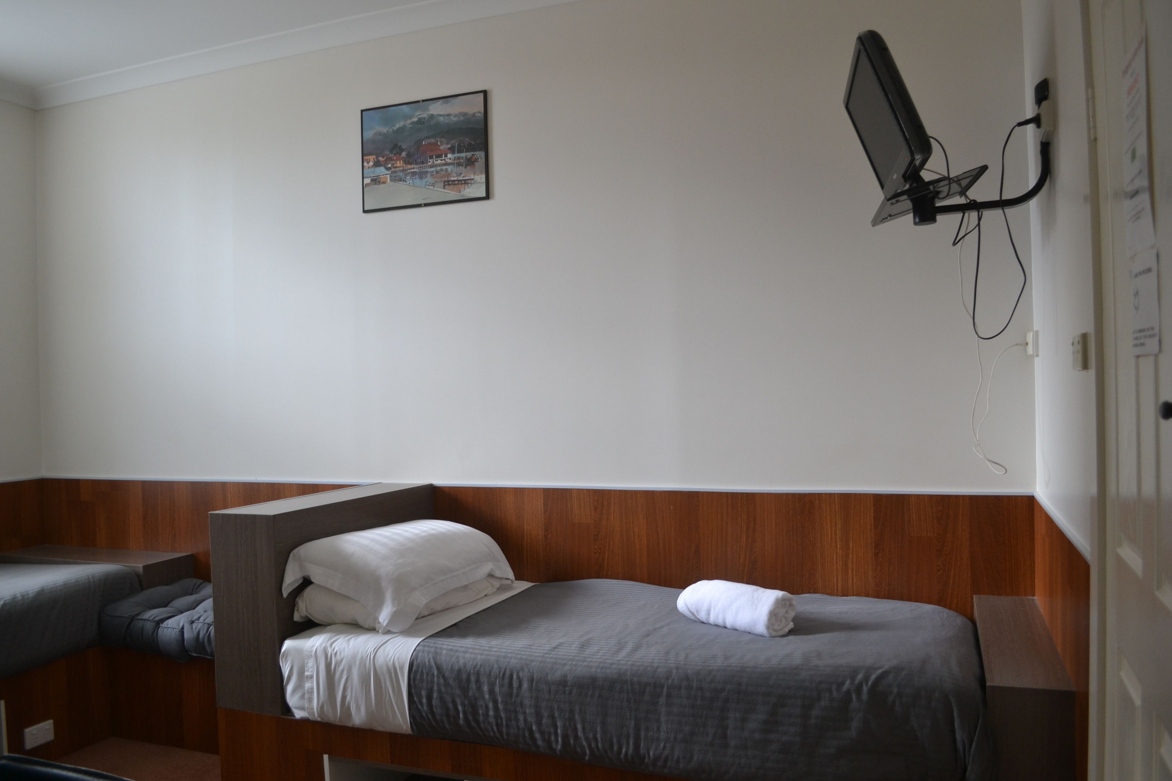 A hotel room with two single beds, a desk, a chair, and a wall-mounted TV.