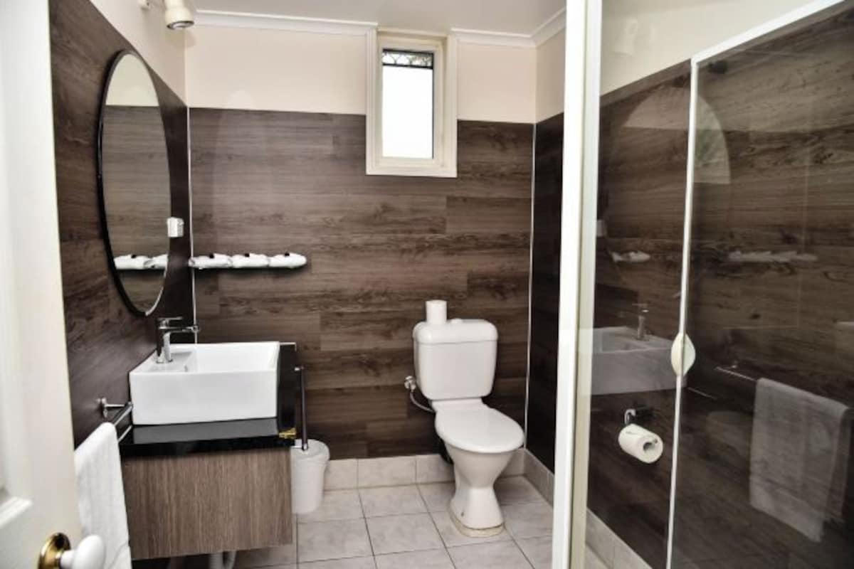 A modern bathroom with a wooden wall, a white sink, a toilet, and a glass shower enclosure.