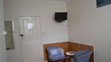 Una stanza con una porta chiusa, una TV a muro, due sedie e un tavolino.