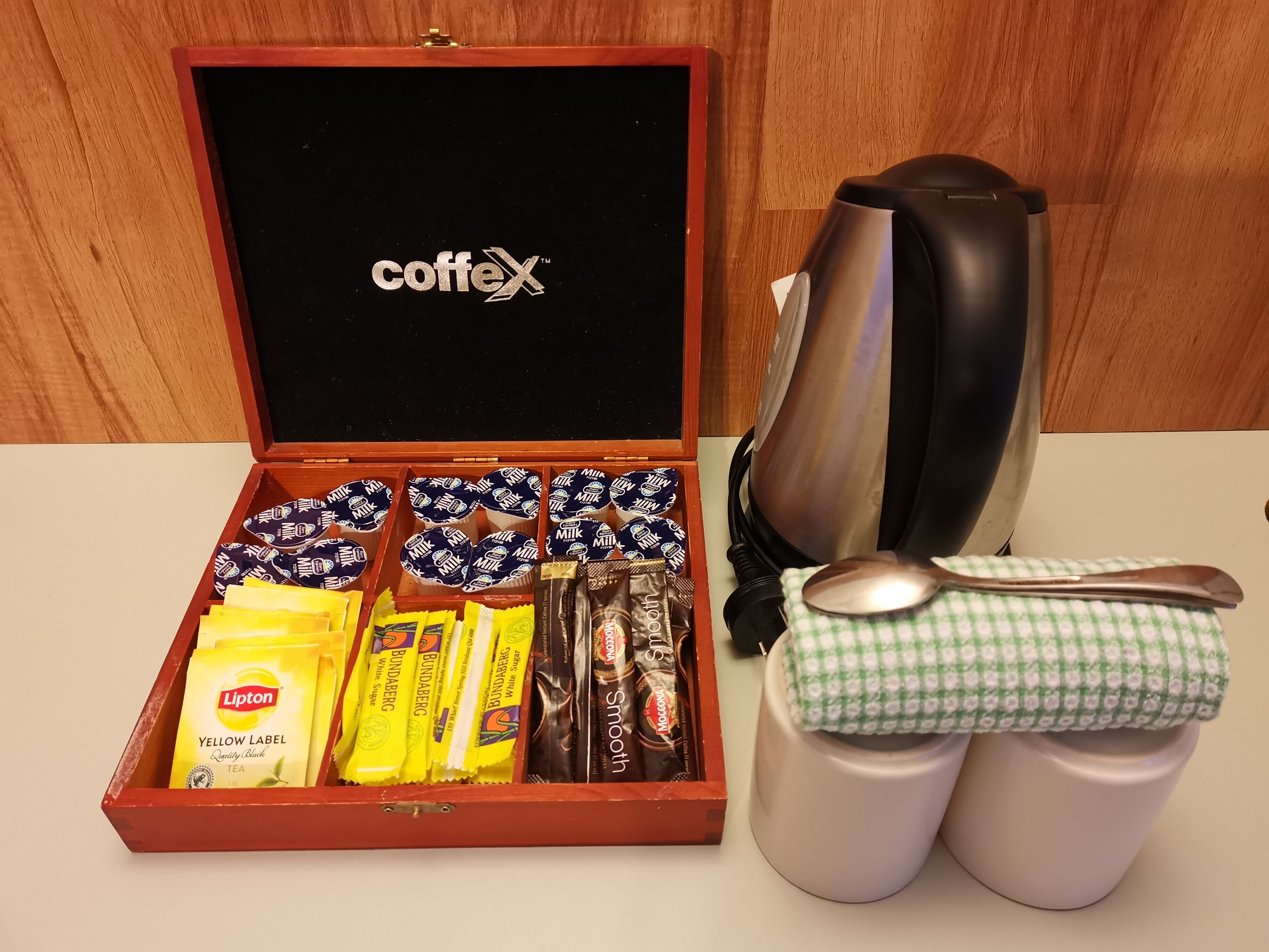 A coffee maker, a spoon, a teapot, and a box of tea and snacks.