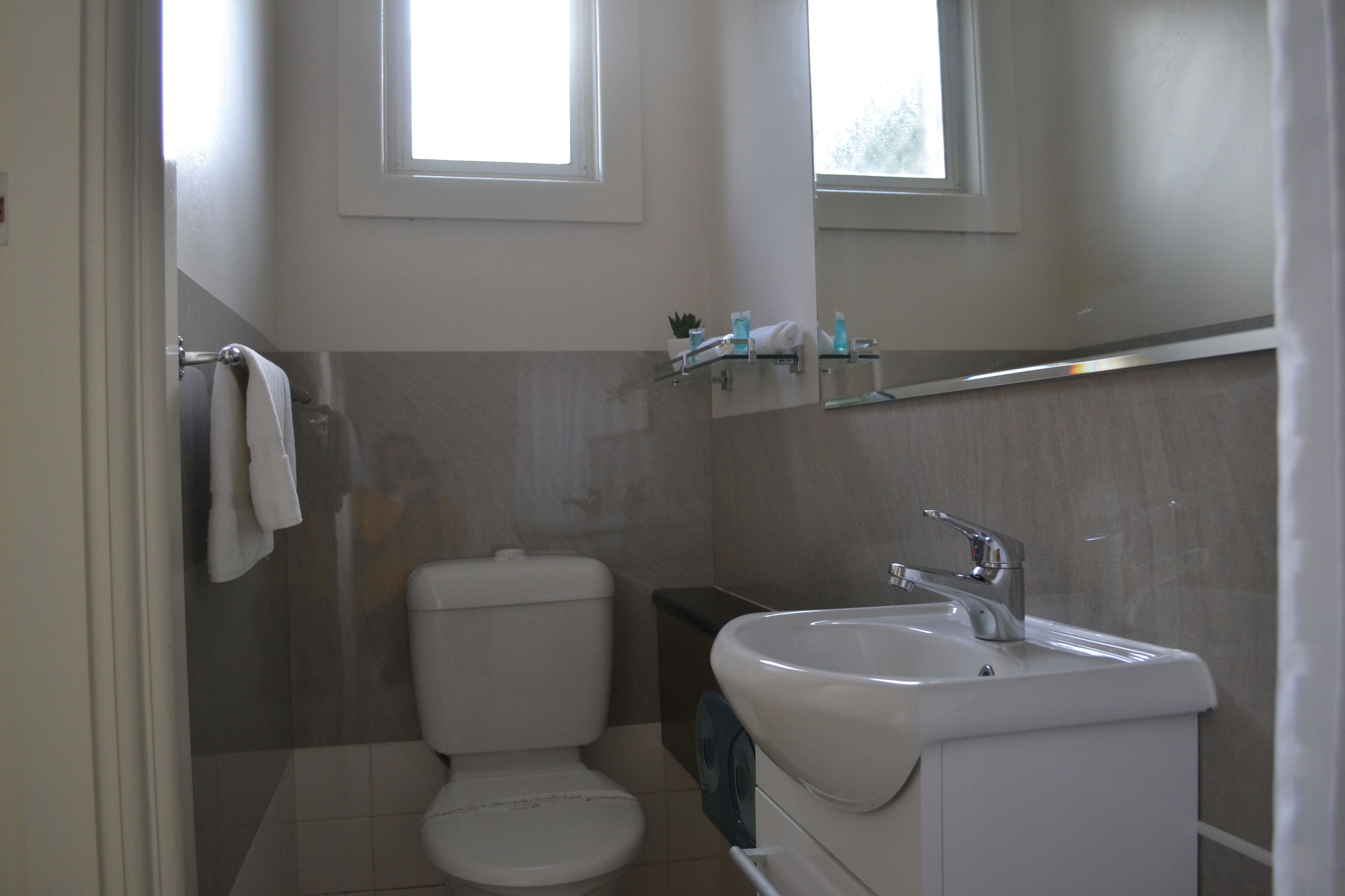 A bathroom with a toilet, sink, and a window above the mirror.