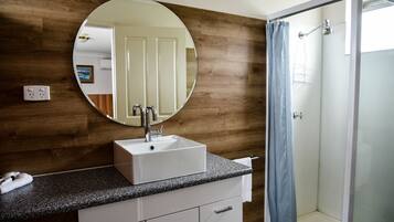 Une salle de bain avec un mur en bois, un miroir rond, un lavabo blanc et une douche avec un rideau bleu.