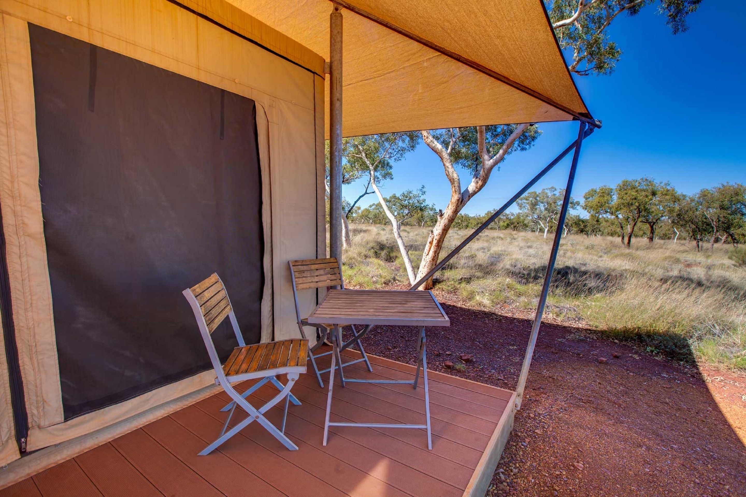 A tent with a table and two chairs on a wooden deck.