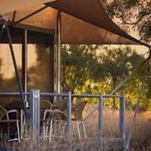 A covered outdoor seating area with metal chairs and a table, surrounded by trees and a fence. - Karijini Eco Retreat (Karijini)