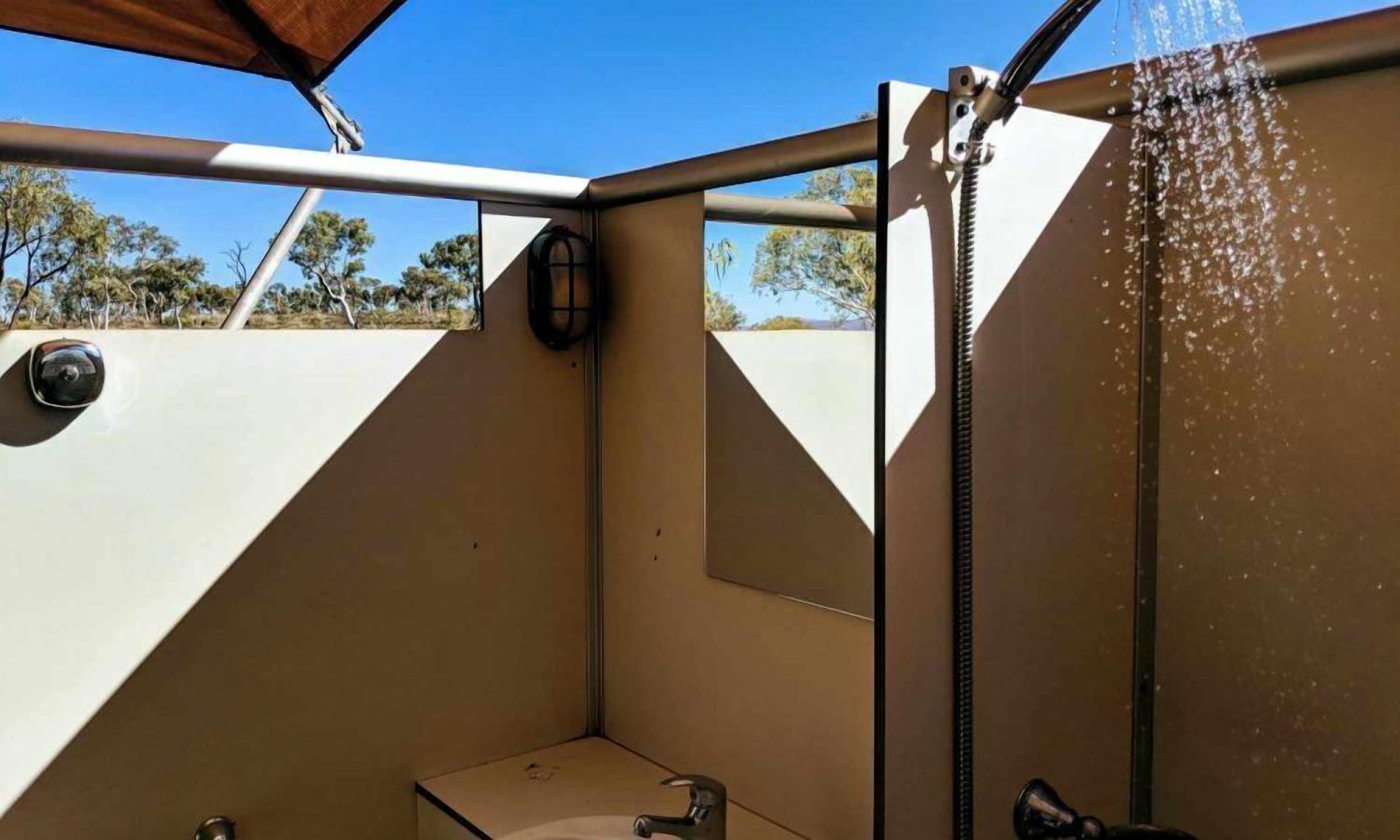 A compact outdoor shower with a hose, a small sink, and a mirror.