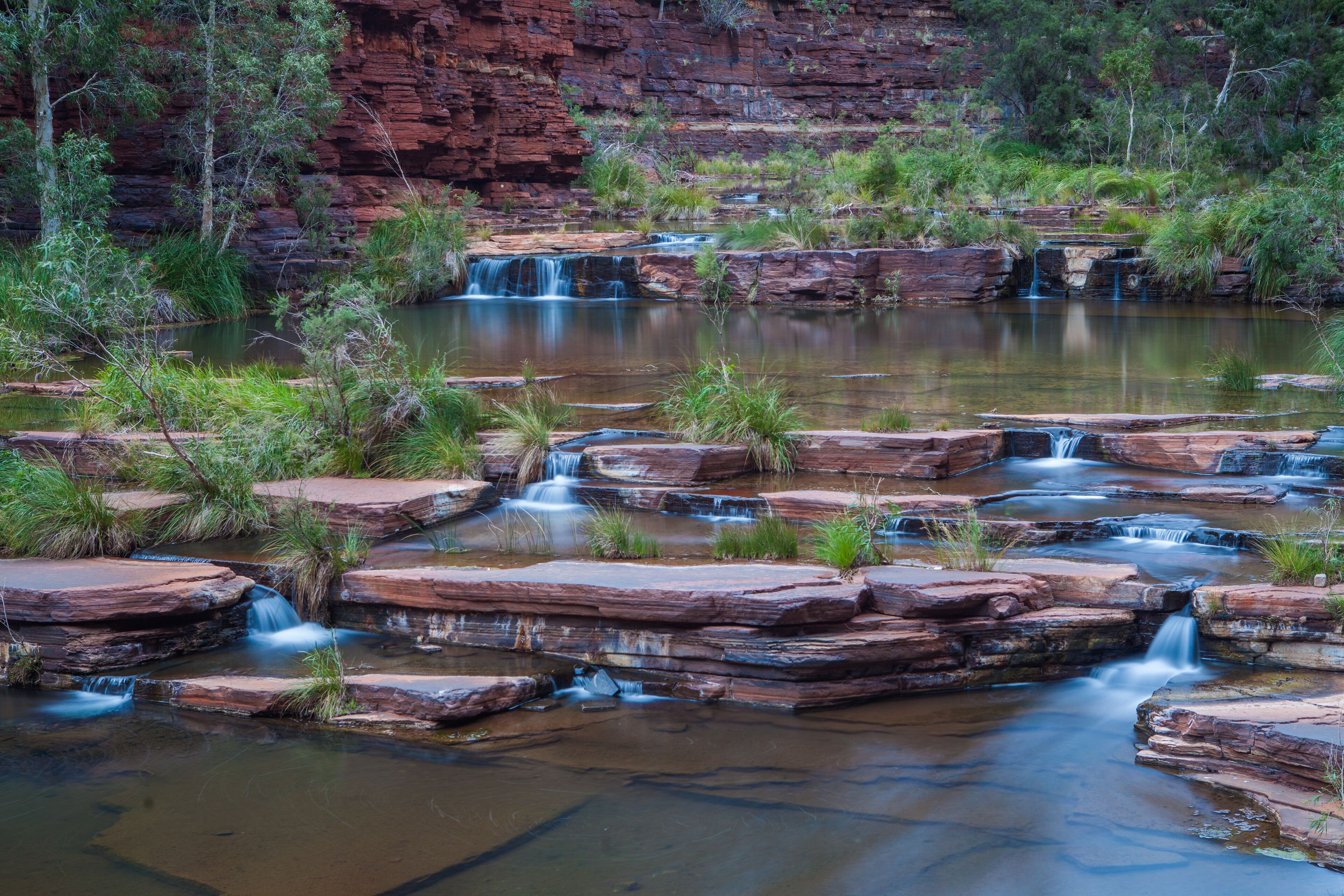 A natural landscape with a series of waterfalls cascading over rocky terrain and a calm body of water.