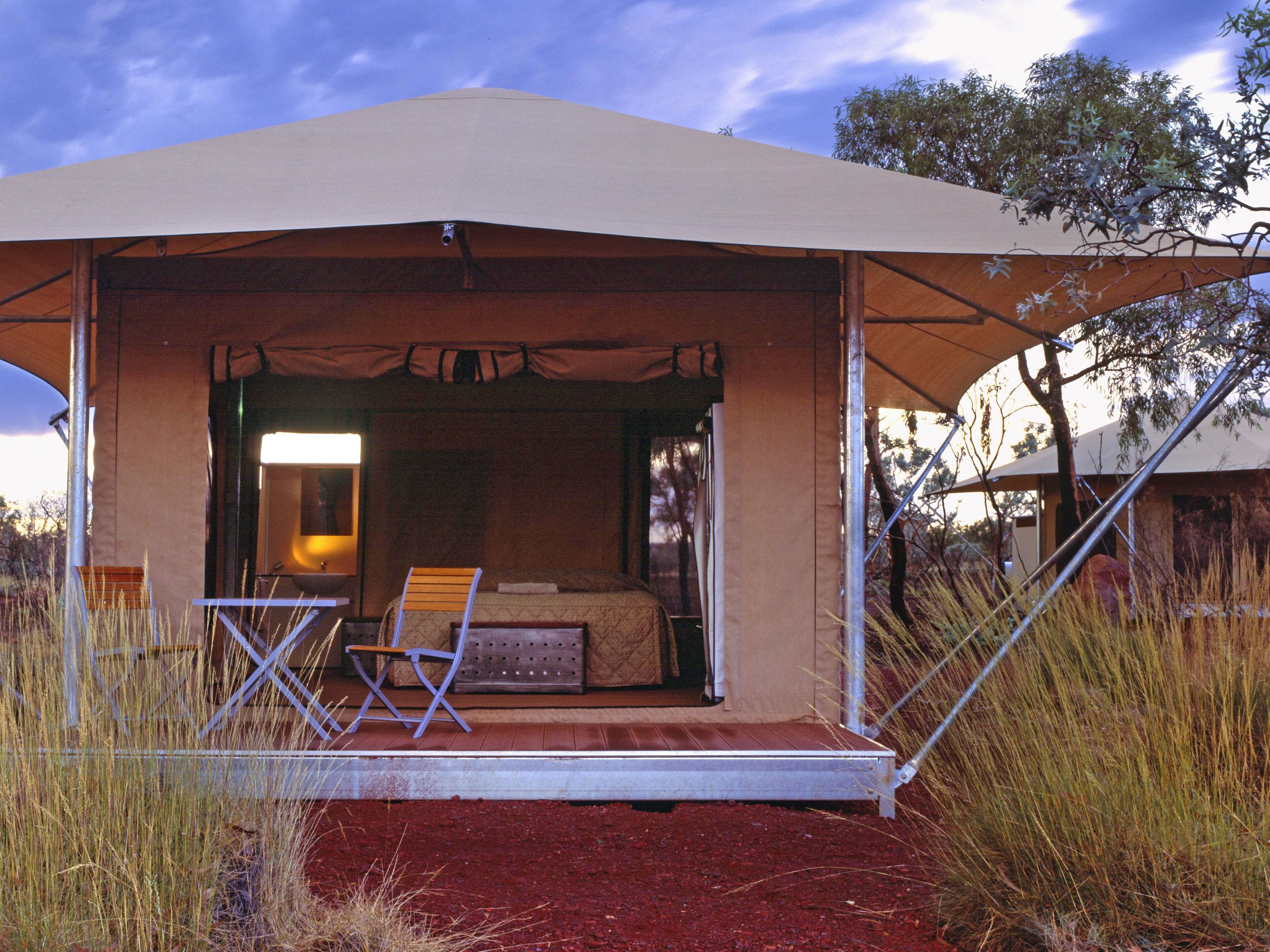 A tented accommodation with a bed, seating area, and a view of the surrounding landscape.