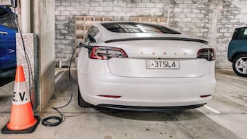 Un Tesla blanco estacionado en un garaje con pared de ladrillo y piso de concreto.