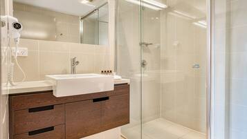 A modern bathroom with a glass-enclosed shower, a white sink, and wooden cabinets.