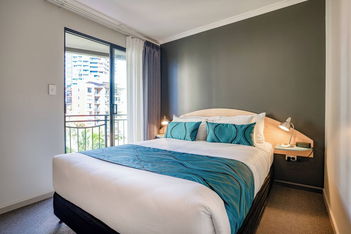 Une chambre d’hôtel avec un grand lit, une table de chevet avec une lampe et une vue sur un immeuble par la fenêtre.