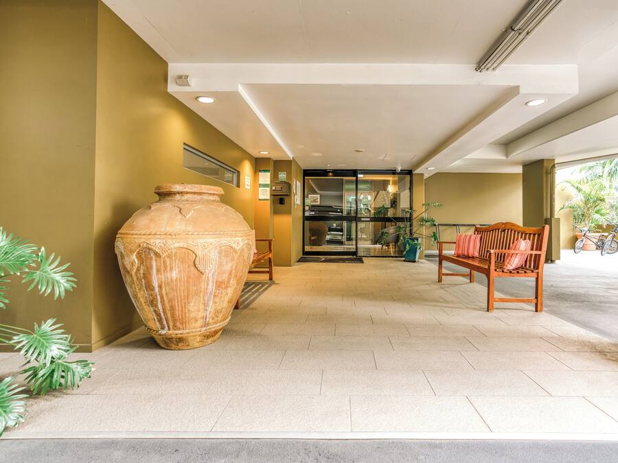 A spacious lobby with a large terracotta pot, a wooden bench, and a glass door leading to a room.