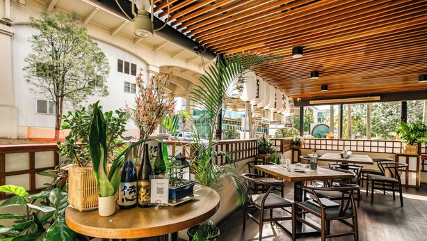 Een restaurant met houten tafels en stoelen, planten in potten en uitzicht op de stad.