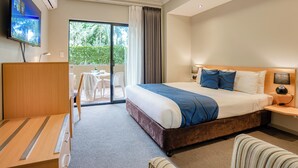 Hotelkamer met een groot bed, een bureau, een stoel, een televisie en een balkon met uitzicht op groen.