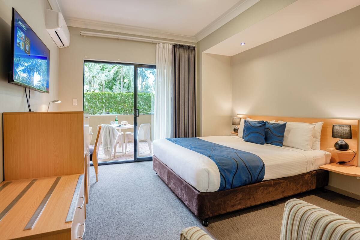 Une chambre d’hôtel avec un grand lit, un bureau, une chaise, une télévision et un balcon donnant sur un espace verdoyant.