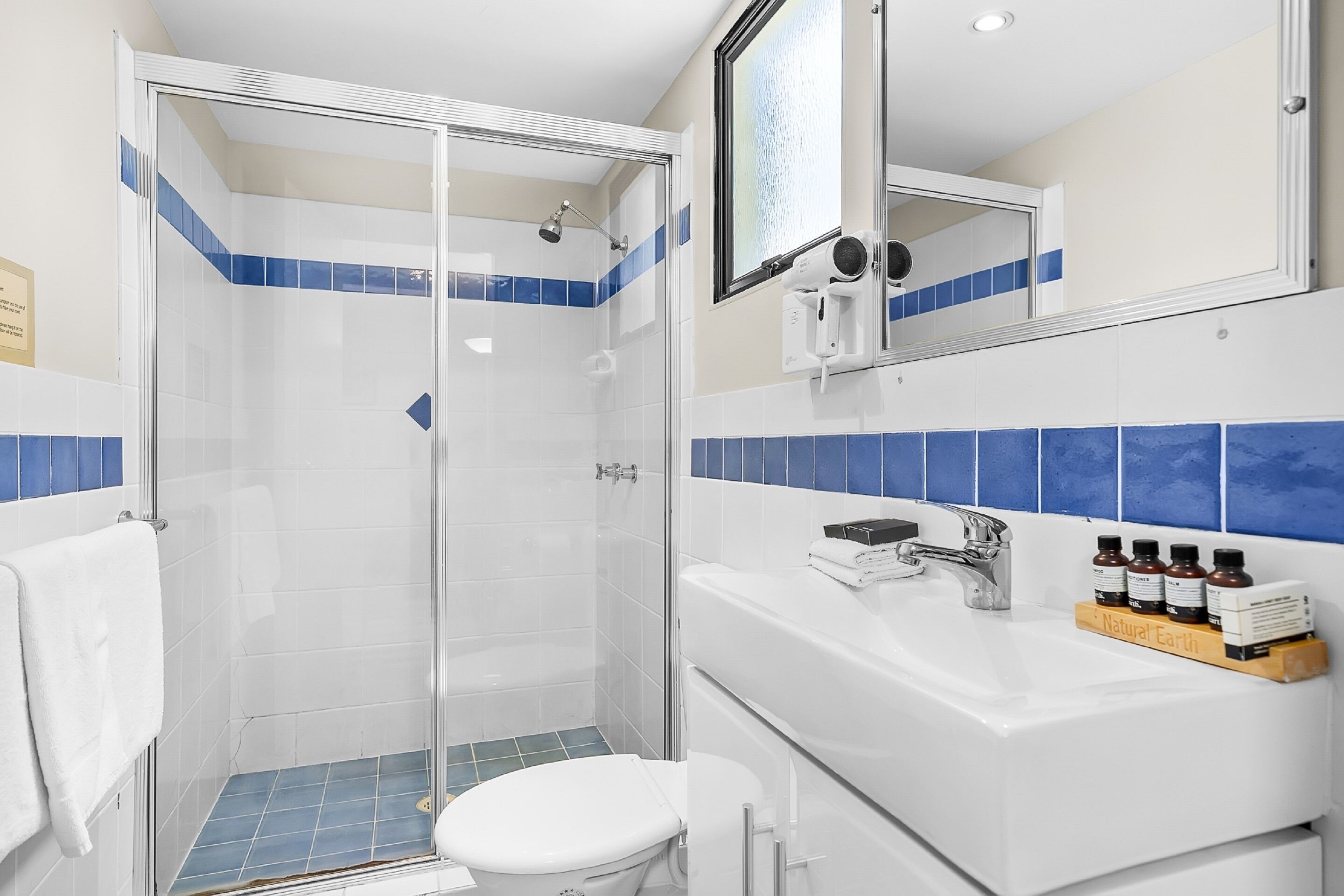 Een badkamer met een douche met glazen wanden, een witte wastafel met zeepdispenser en een spiegel boven de wastafel.