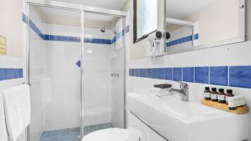 Een badkamer met een douche met glazen wanden, een witte wastafel met zeepdispenser en een spiegel boven de wastafel.