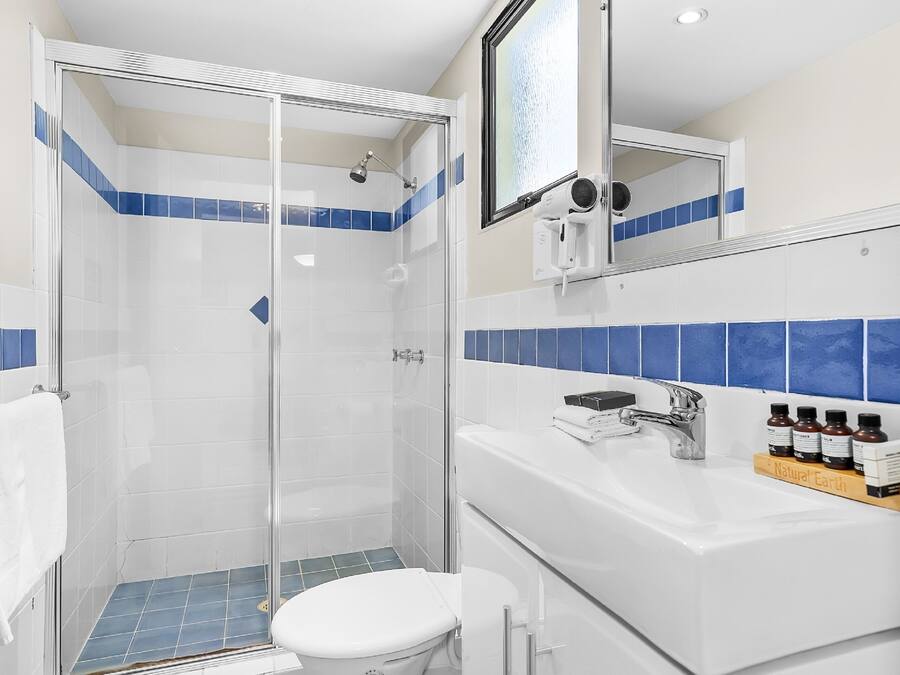 Een badkamer met een douche met glazen wanden, een witte wastafel met zeepdispenser en een spiegel boven de wastafel.
