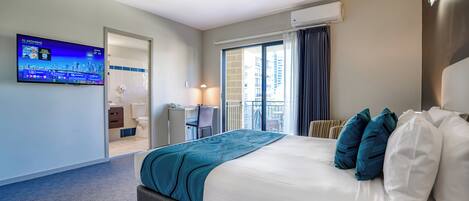 Habitación de hotel con cama, escritorio, televisión y balcón con cortinas.