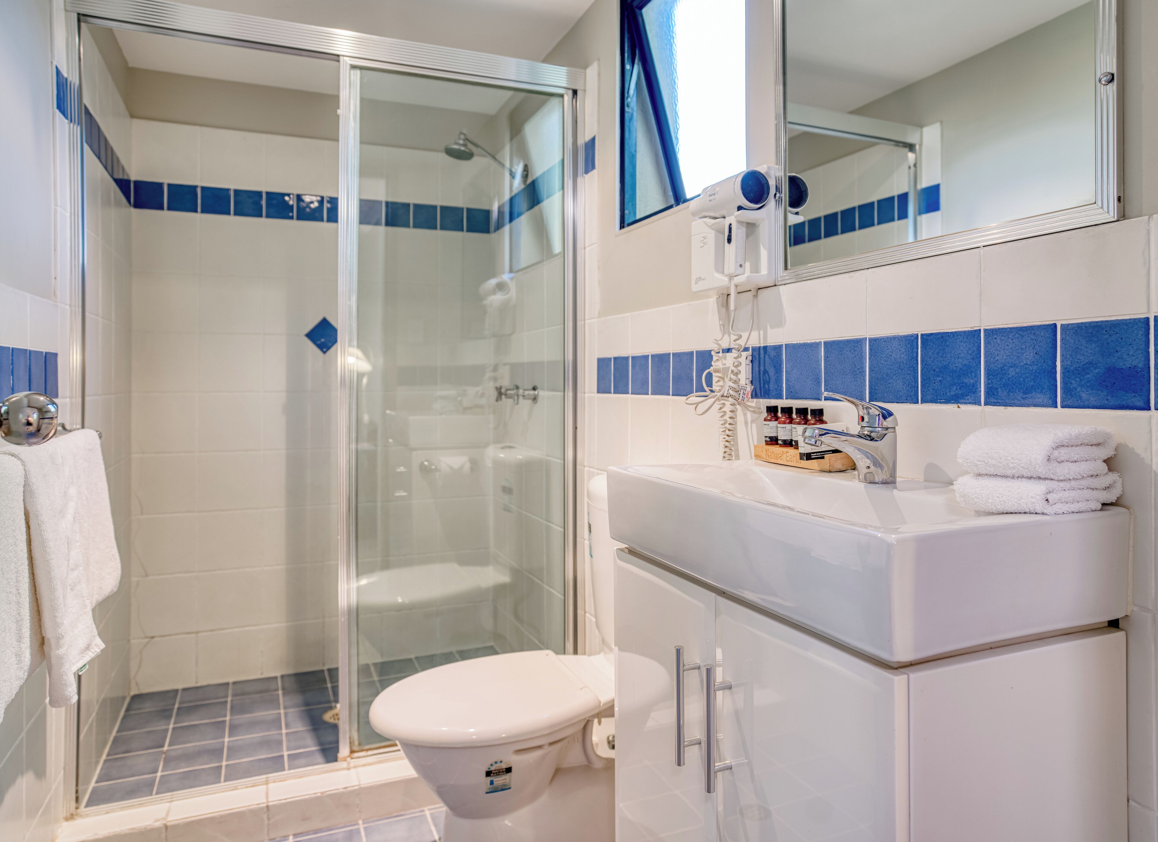 A bathroom with a glass shower enclosure, a white toilet, and a sink with a mirror above it.