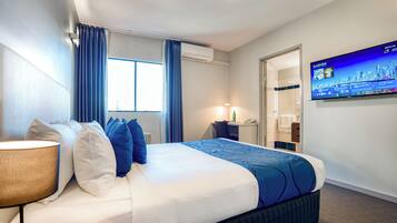 Een hotelkamer met een bed, een televisie, een lamp en een raam met gordijnen.