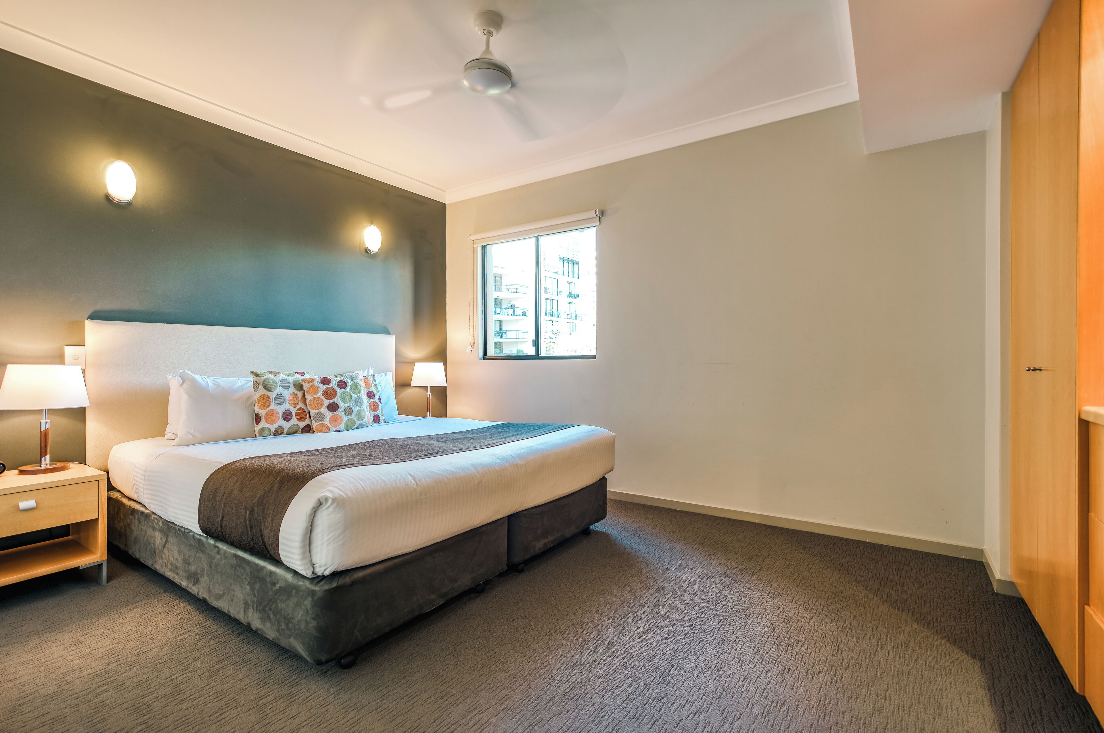 Een slaapkamer met een bed, nachtkastjes, een plafondventilator, een raam en een deur.