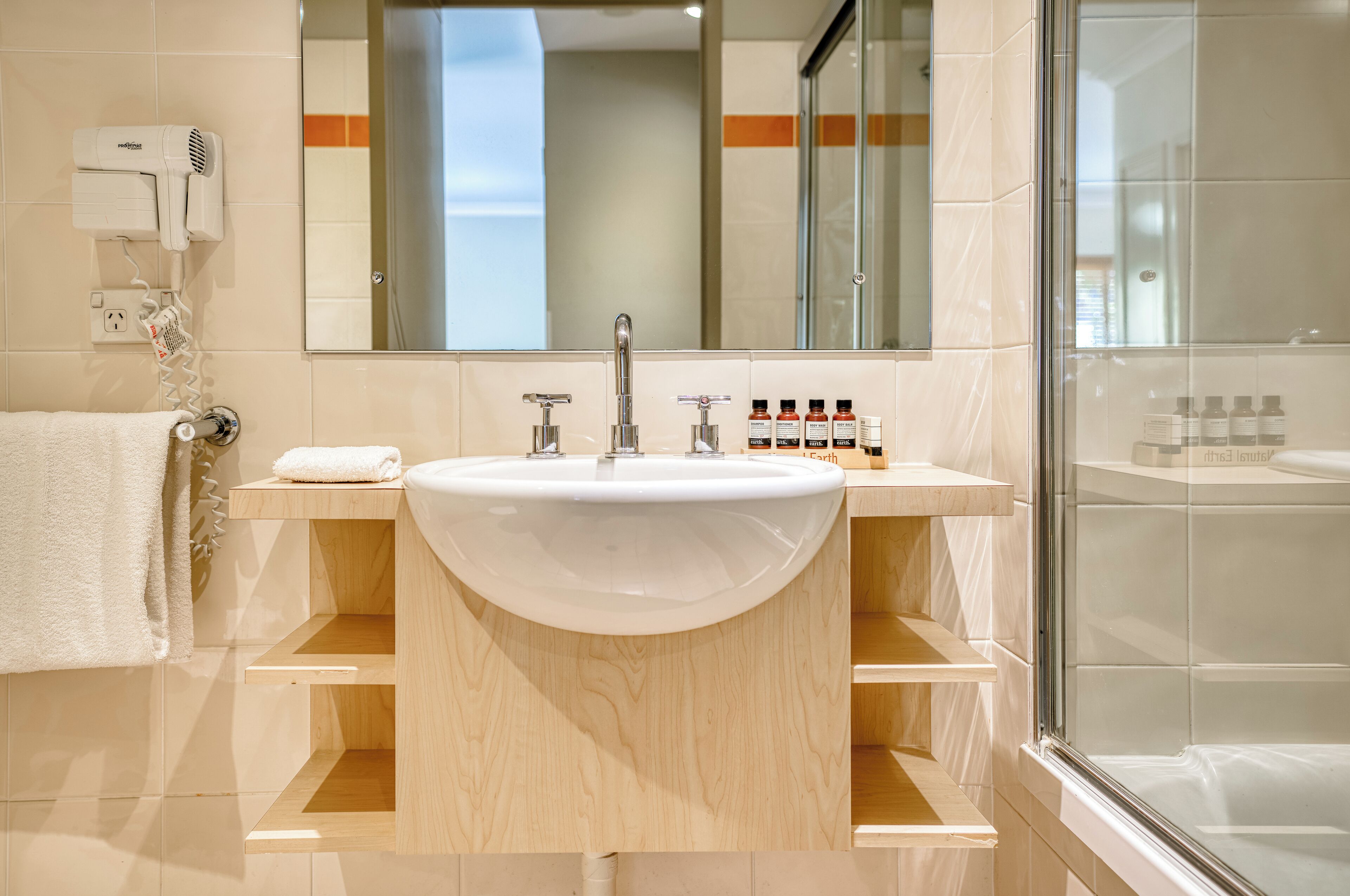 Un baño moderno con un lavamanos grande, un secador de pelo y una cabina de ducha de vidrio.