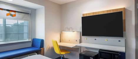 A hotel room with a bed, a desk with a chair, a flat-screen TV, a microwave, and a window with a view.