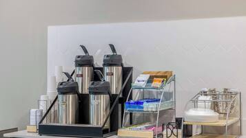 A coffee station with two espresso machines, a coffee dispenser, and a milk frother. There are disposable cups and a coffee grinder on the counter.
