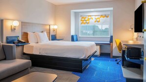 A modern hotel room with a bed, bedside tables, a desk, a chair, and a large window with a geometric curtain. - Microtel Inn & Suites by Wyndham Anderson/Clemson (Anderson)