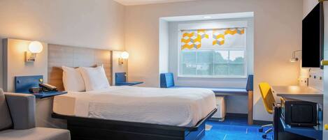 A modern hotel room with a bed, bedside tables, a desk, a chair, and a large window with a geometric curtain.