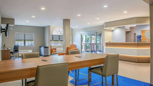 A modern hotel lobby with a reception desk, seating area, and a large conference table. - Microtel Inn & Suites by Wyndham Anderson/Clemson (Anderson)