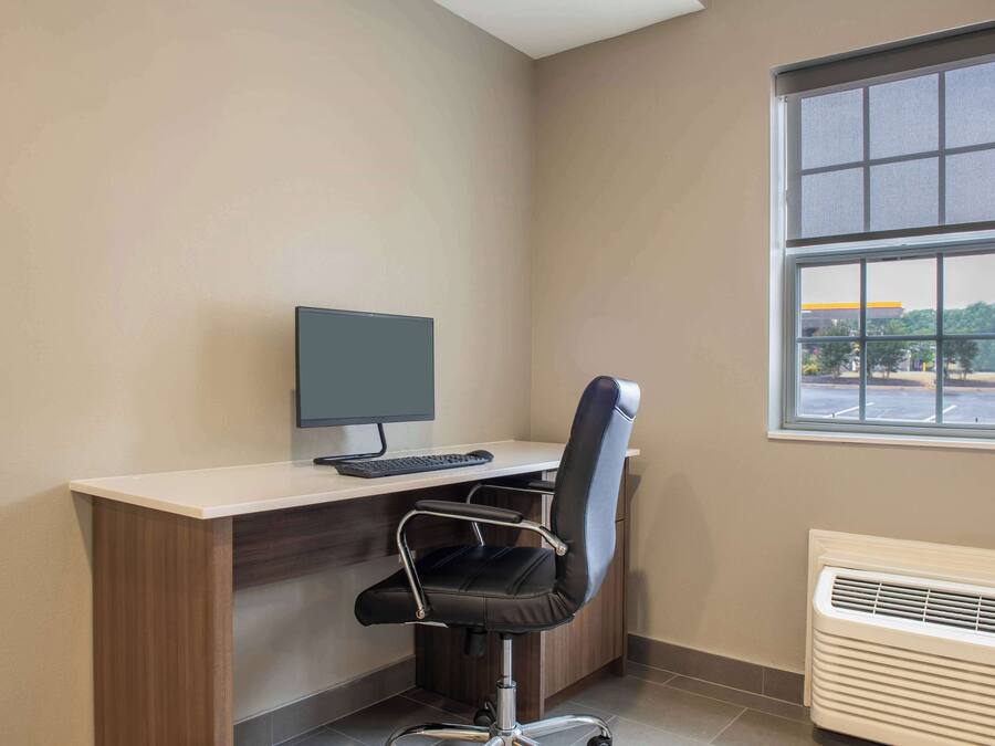 A corner office with a desk, chair, computer, and window.