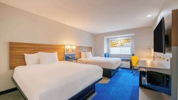 A hotel room with two beds, a desk with a flat-screen TV, a microwave, and a window with a geometric pattern.