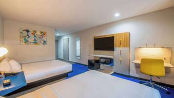 A hotel room with two beds, a desk with a lamp, a TV, a microwave, and a small cabinet.